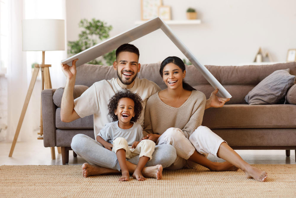 cheerful parents with child smiling keeping roof mockup heads while sitting floor cozy living room during relocation1